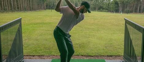 A golf course with a player in a white shirt and dark pants preparing to swing.