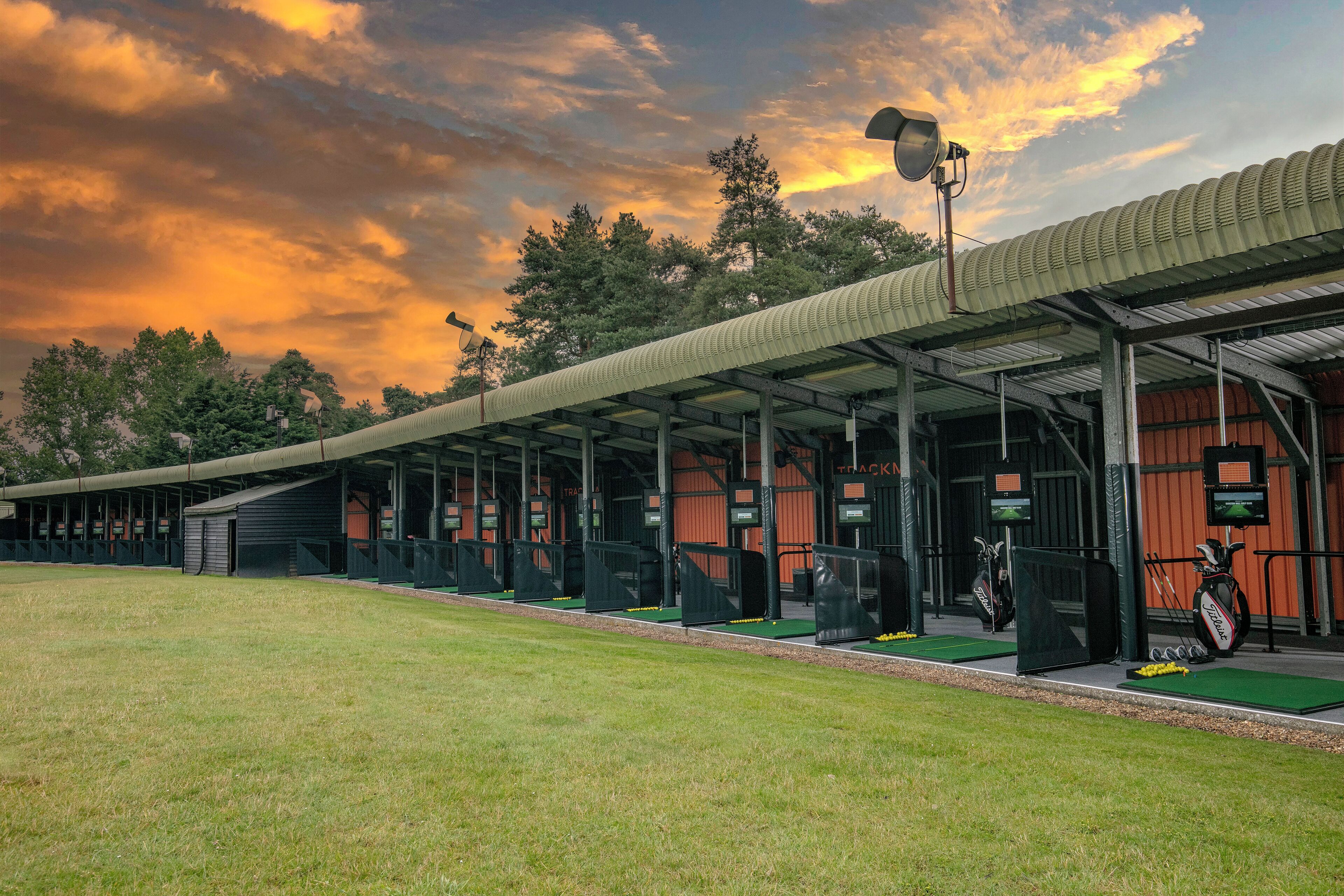 A golf driving range with multiple tee boxes, a covered seating area, and a clear sky.
