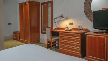 A bedroom with a bed, wooden wardrobe, desk with chair, desk lamp, mirror, and a television.