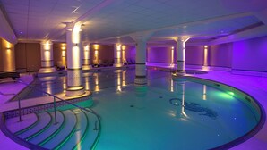Una amplia piscina interior con múltiples carriles, rodeada de zonas de estar e iluminada con luz ambiental.
