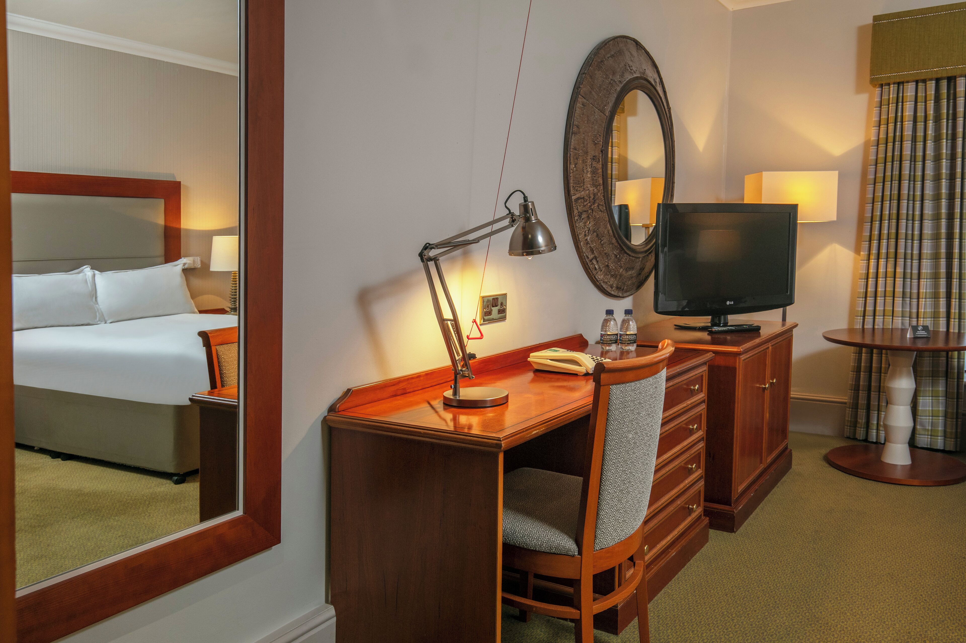 Una habitación de hotel con cama, escritorio, silla, televisor y espejo.