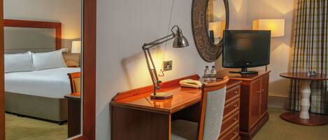 Una habitación de hotel con cama, escritorio, silla, televisor y espejo.