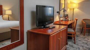 Habitación de hotel con escritorio de madera, televisor, lámpara, silla y cama.