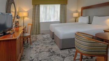 Una habitación de hotel con cama, escritorio con televisor, silla y ventana con cortinas.