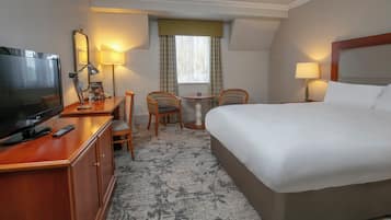 Habitación de hotel con cama, escritorio con televisor, silla, mesita y lámpara.