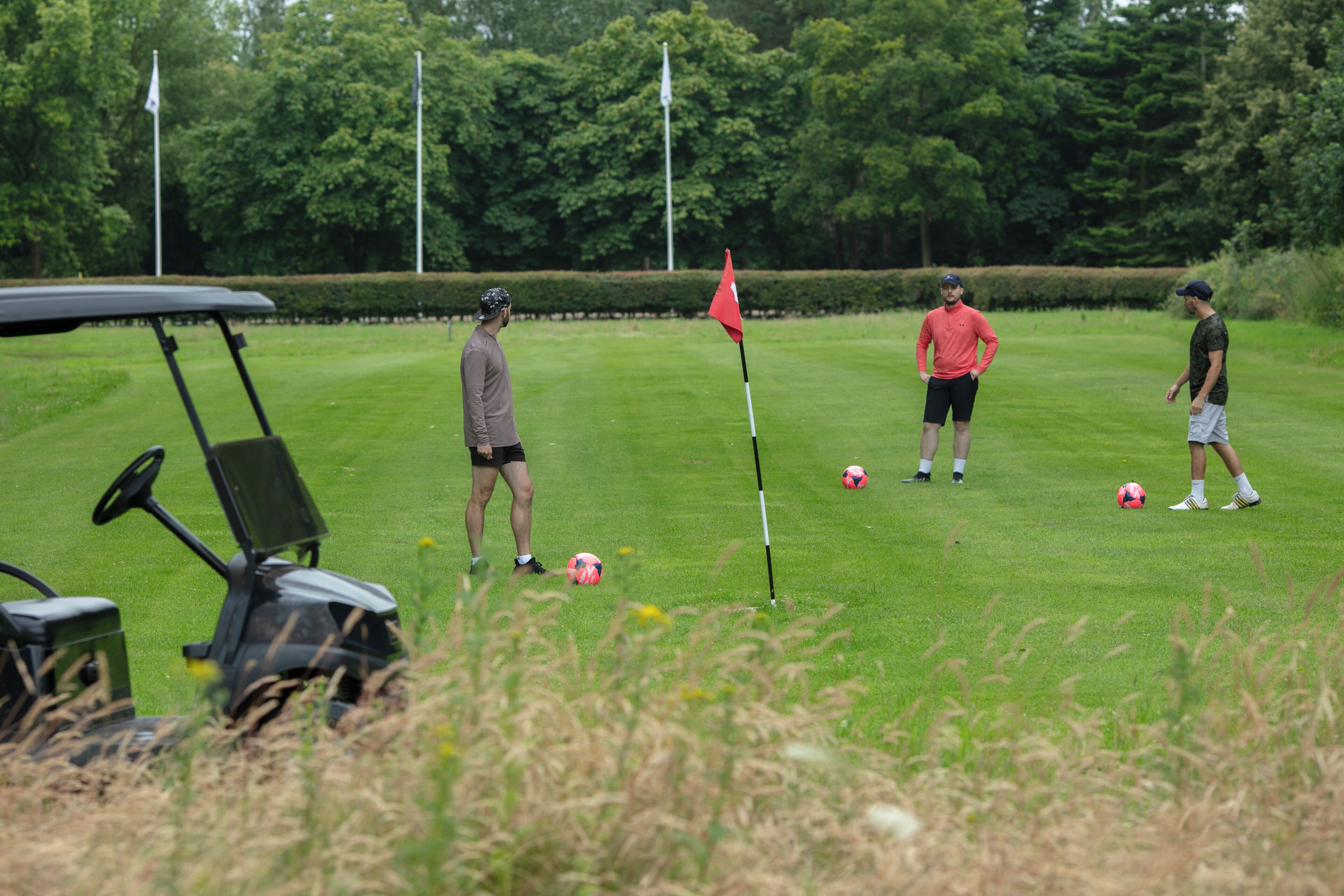 A golf course with a flag, golf cart, and players.