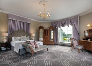 A bedroom with a large bed, two bedside tables, a dresser, a vanity, a mirror, and a chandelier. - Castle Oaks House Hotel (Castleconnell)