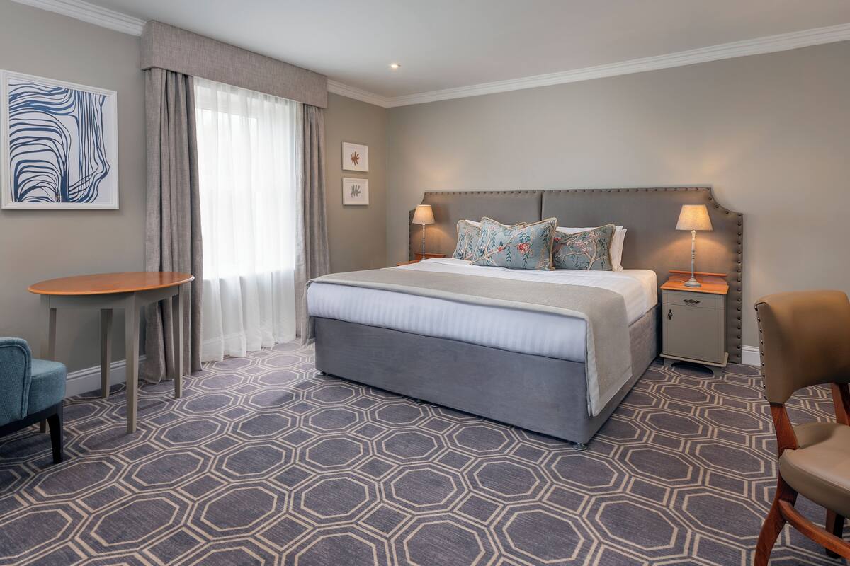 A hotel room with a large bed, a bedside table, a chair, and a small table.