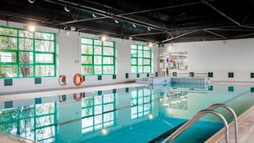 A swimming pool with clear blue water, surrounded by white walls and large windows with green frames.