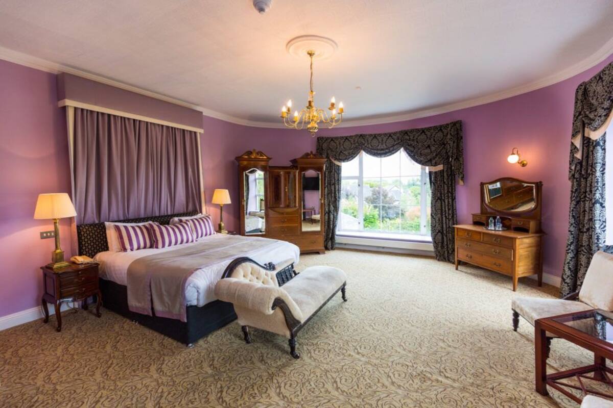 A bedroom with a large bed, a nightstand, a dresser, a chair, and a window with curtains.
