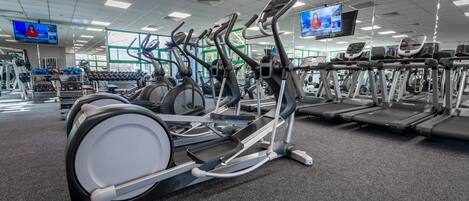 A gym with multiple exercise machines, including treadmills and elliptical trainers, arranged in rows.