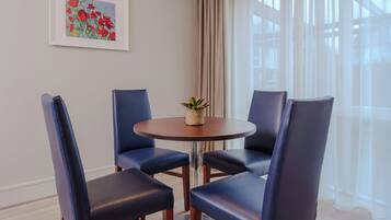 A room with a round table, four blue chairs, a framed painting, and a window with curtains.