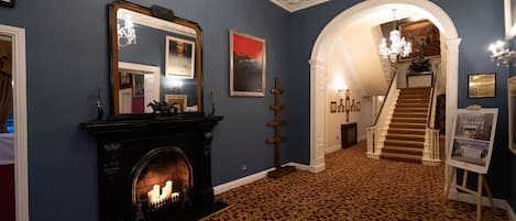 A grand hallway with a fireplace, a staircase, and a chandelier.
