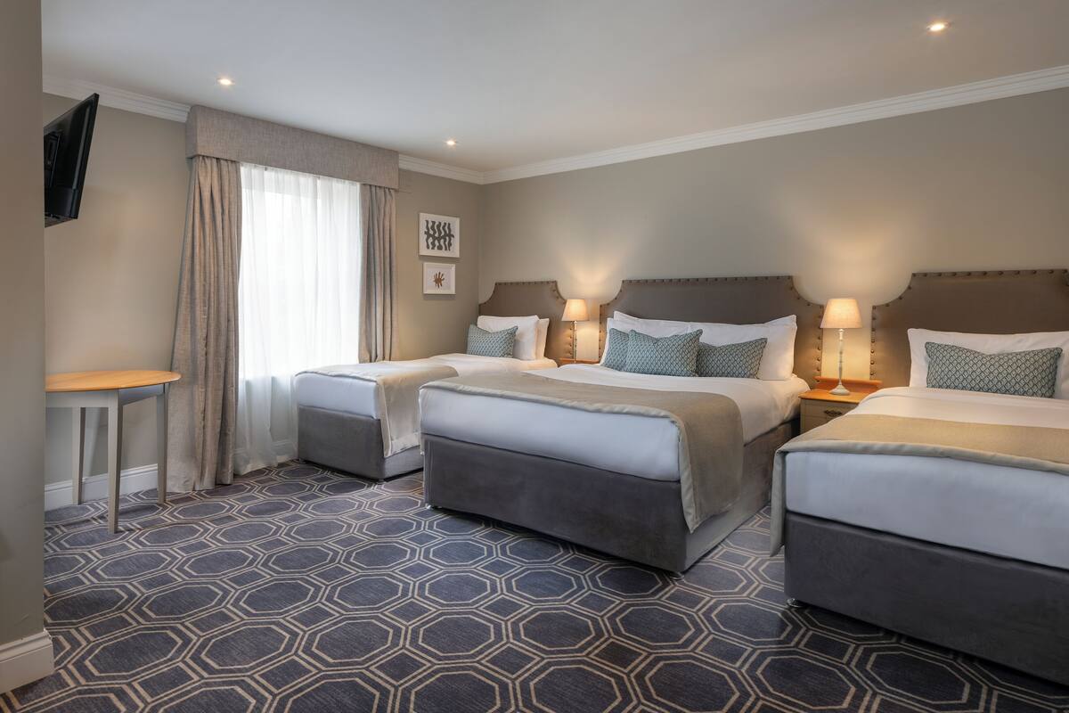A hotel room with two beds, a small table, and a TV mounted on the wall.