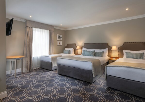 A hotel room with two beds, a small table, and a TV mounted on the wall. - Castle Oaks House Hotel (Castleconnell)