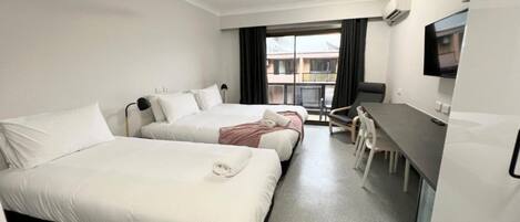 A hotel room with two beds, a desk, a chair, a TV, and a ceiling fan.