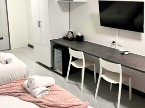 A hotel room with a bed, a desk with two chairs, a television, and a minibar.