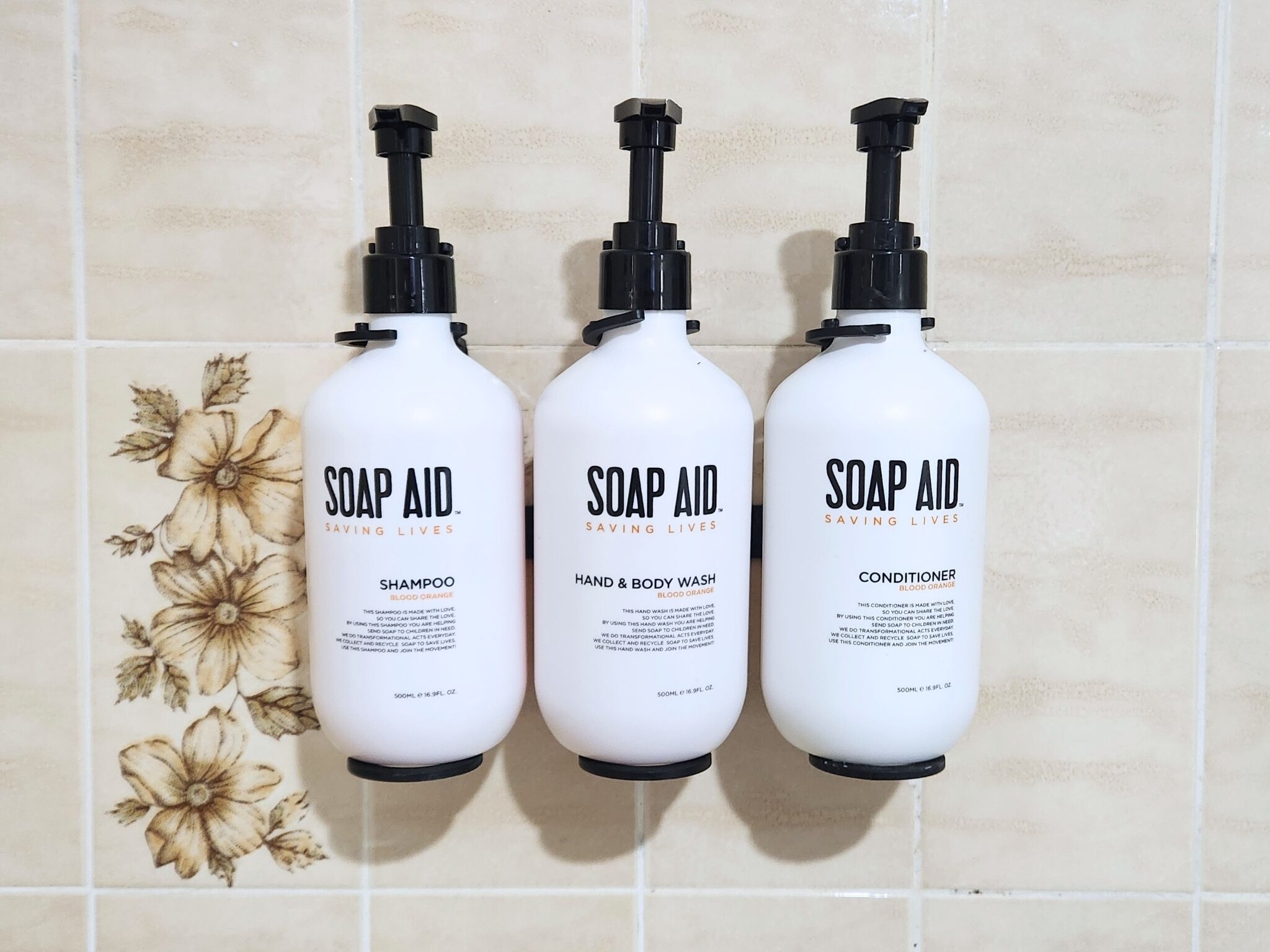 Trois bouteilles de produits Soap Aid sont posées contre un mur carrelé.