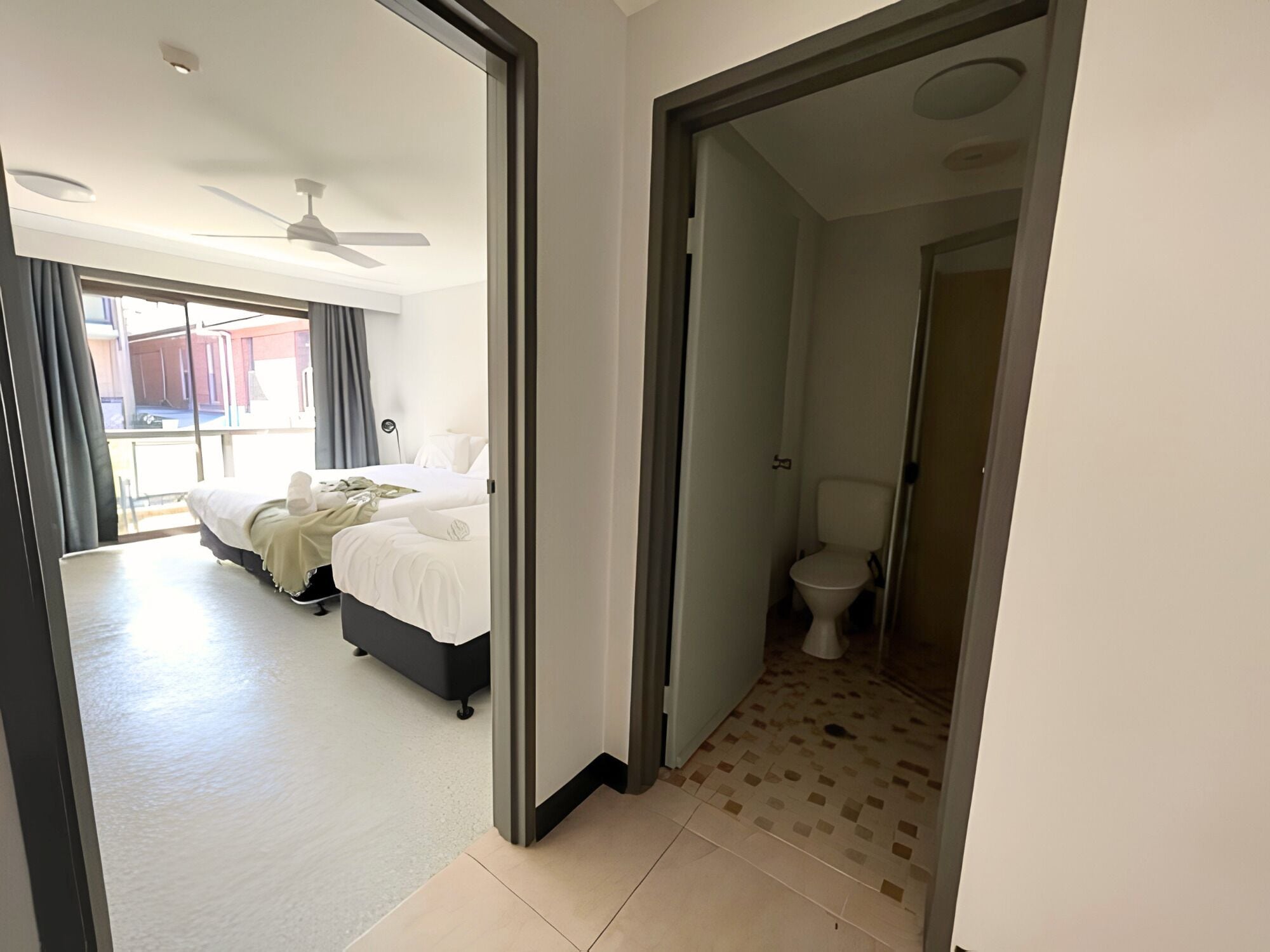 A hotel room with a bed, a bathroom, and a view of the outside.