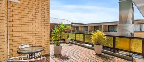 A balcony with a tiled floor, potted plants, and a table with chairs.