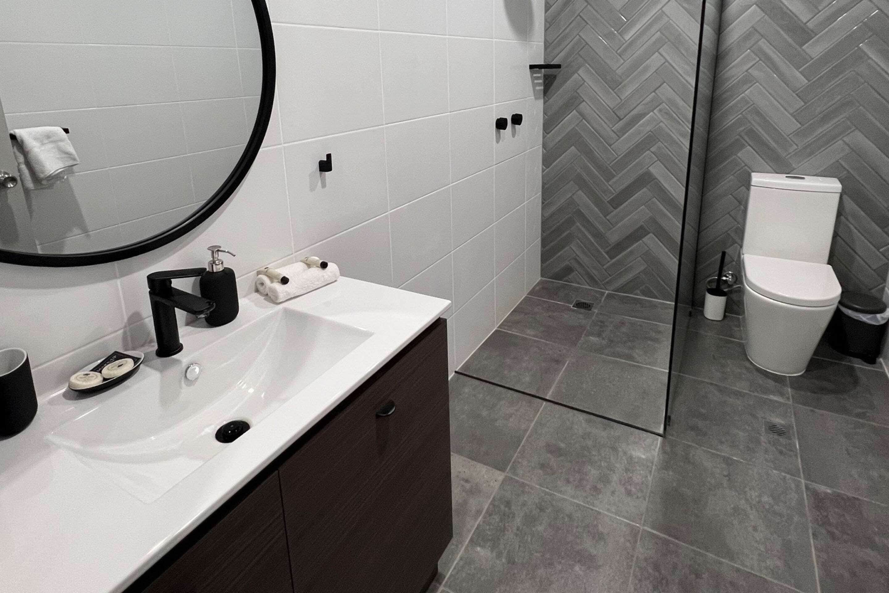 A modern bathroom with a white sink, dark cabinet, and a mirror.