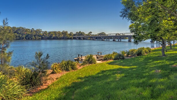 A lakeside view with a bridge, grassy areas, and a picnic table. - Pleasant Way River Lodge (Nowra)