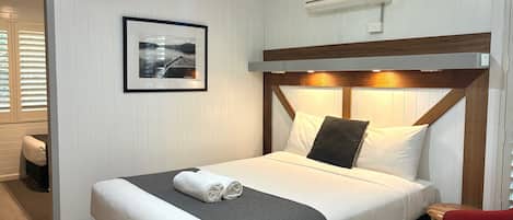Una cama bien hecha con ropa de cama blanca y gris, un cabecero de madera y un cuadro en la pared.