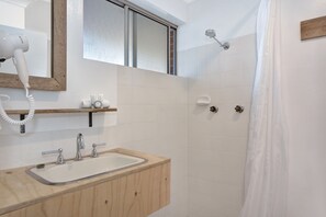 A bathroom with a wooden vanity, a hairdryer, a mirror, and a shower with a curtain.