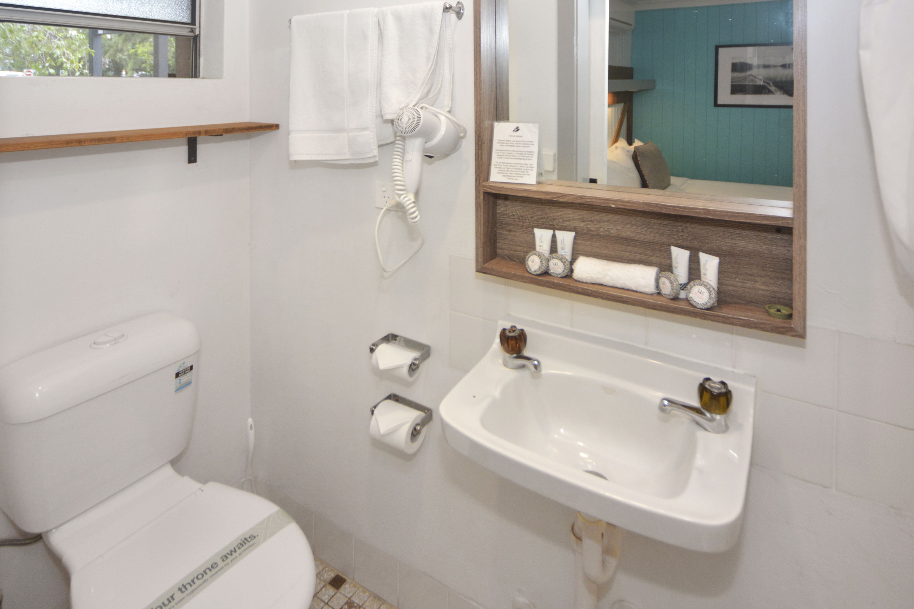 A bathroom with a toilet, a sink, a hairdryer, and a mirror.