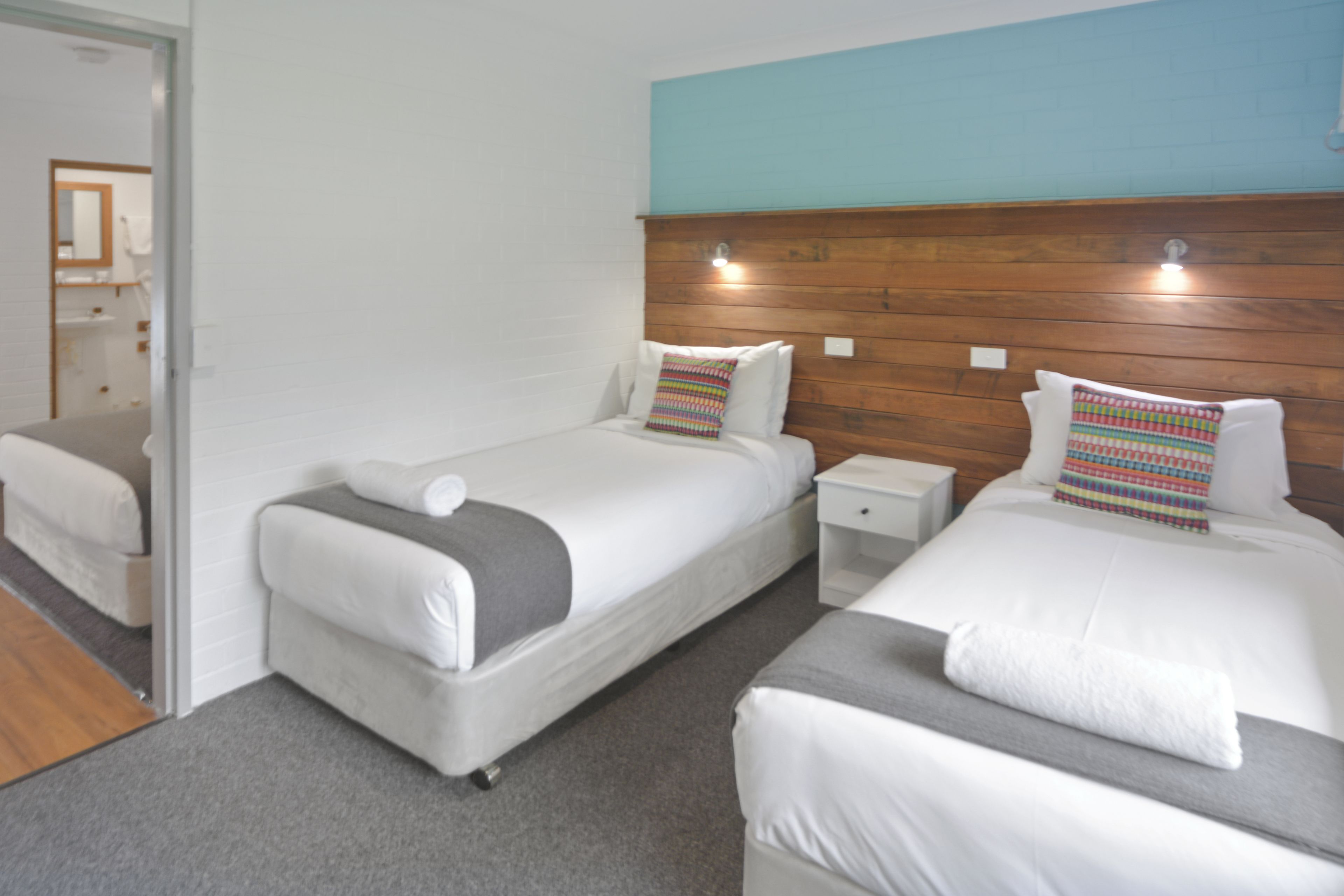 A hotel room with two beds, a wooden headboard, and a small bedside table.