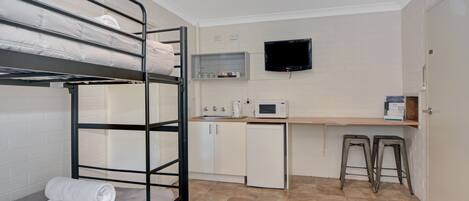 A bunk bed with a white towel, a microwave, a small refrigerator, a TV, and a wooden desk with two stools.