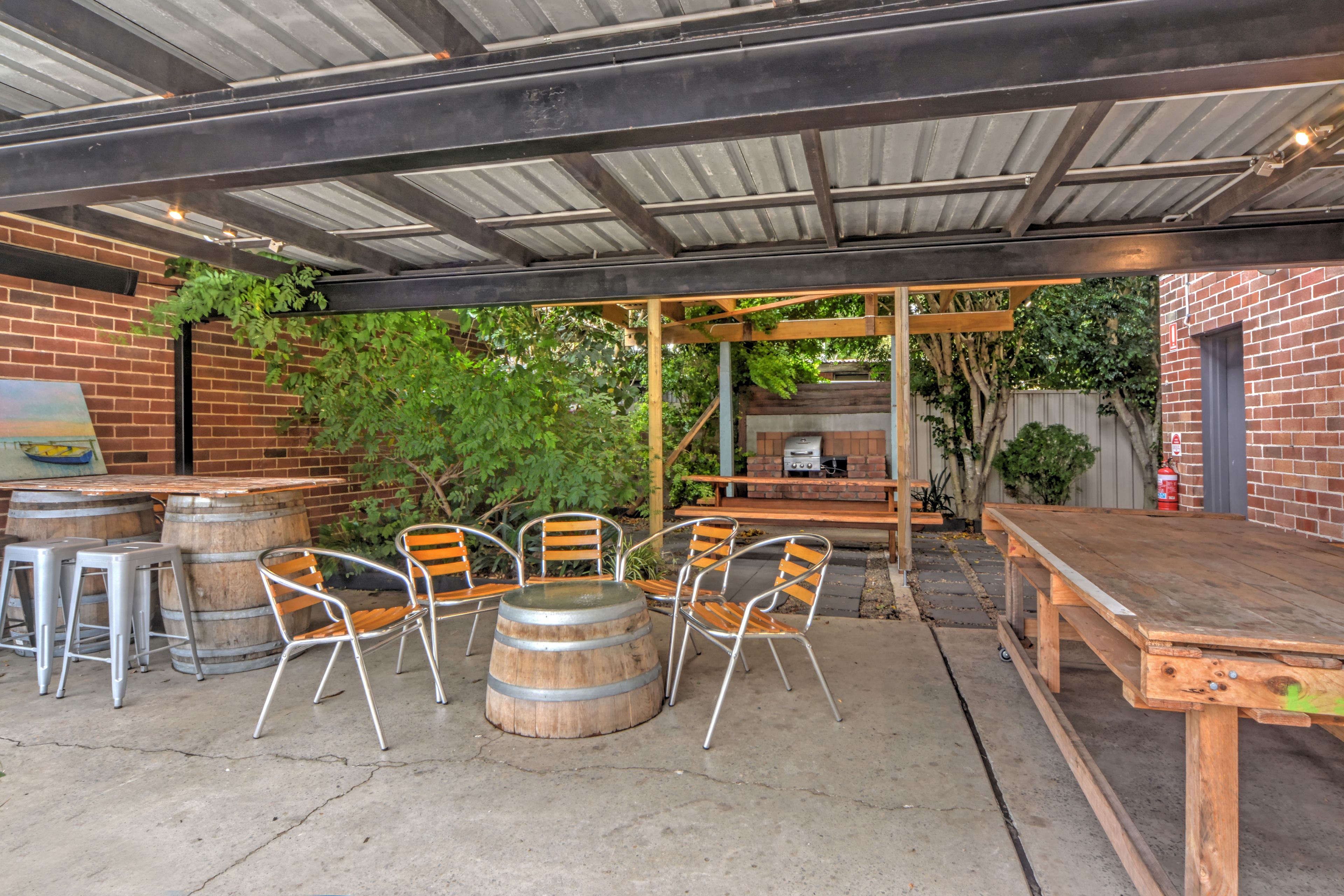 An outdoor patio with a wooden table and chairs, a barbecue grill, and a brick wall.