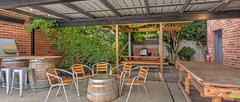 Un patio al aire libre con una mesa y sillas de madera, una parrilla de barbacoa y un muro de ladrillo.