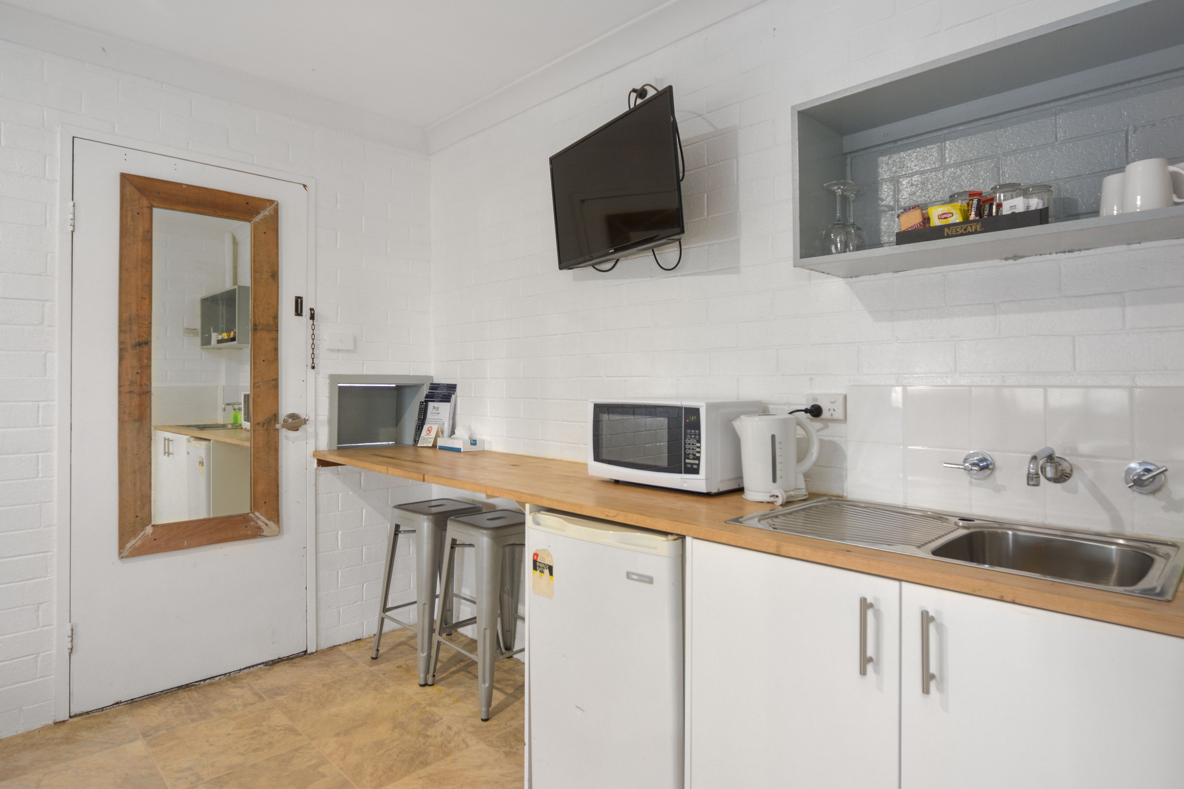 A compact kitchen with white brick walls, a wooden countertop, a microwave, a coffee maker, and a sink.