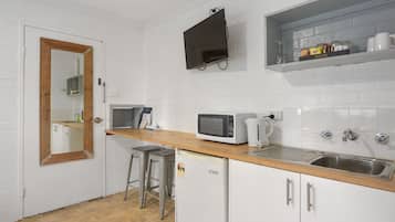 A compact kitchen with white brick walls, a wooden countertop, a microwave, a coffee maker, and a sink.