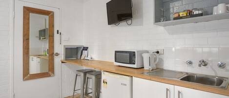 A compact kitchen with white brick walls, a wooden countertop, a microwave, a coffee maker, and a sink.