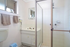 Bathroom features a sink, mirror, glass-enclosed shower, and a small window.