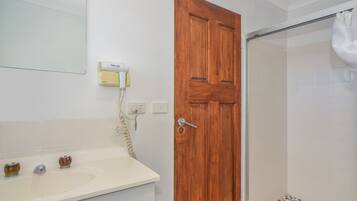 Un baño con puerta de madera, un lavabo blanco con dos grifos y una zona de ducha con puerta de cristal.
