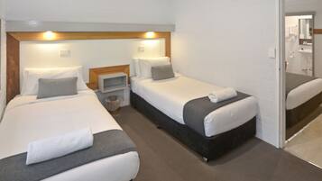 Quarto de hotel com duas camas de solteiro, uma pequena mesa de cabeceira e um banheiro visível através de uma porta aberta.