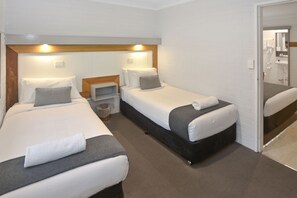 A hotel room with two single beds, a small bedside table, a nightstand, and a bathroom visible through an open door.