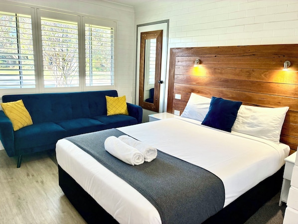 A hotel room with a bed, a blue sofa, and a wooden headboard.