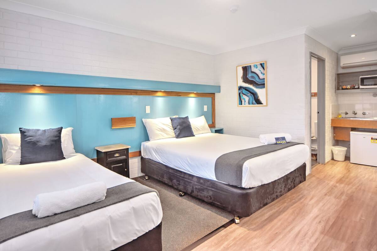 A hotel room with two beds, a kitchenette, and a bathroom.