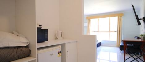 A compact hotel room with a kitchenette, a bed, a small desk, and a window with curtains.