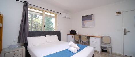 Habitación de hotel con cama, escritorio, silla, mesita de noche y ventana con cortinas.