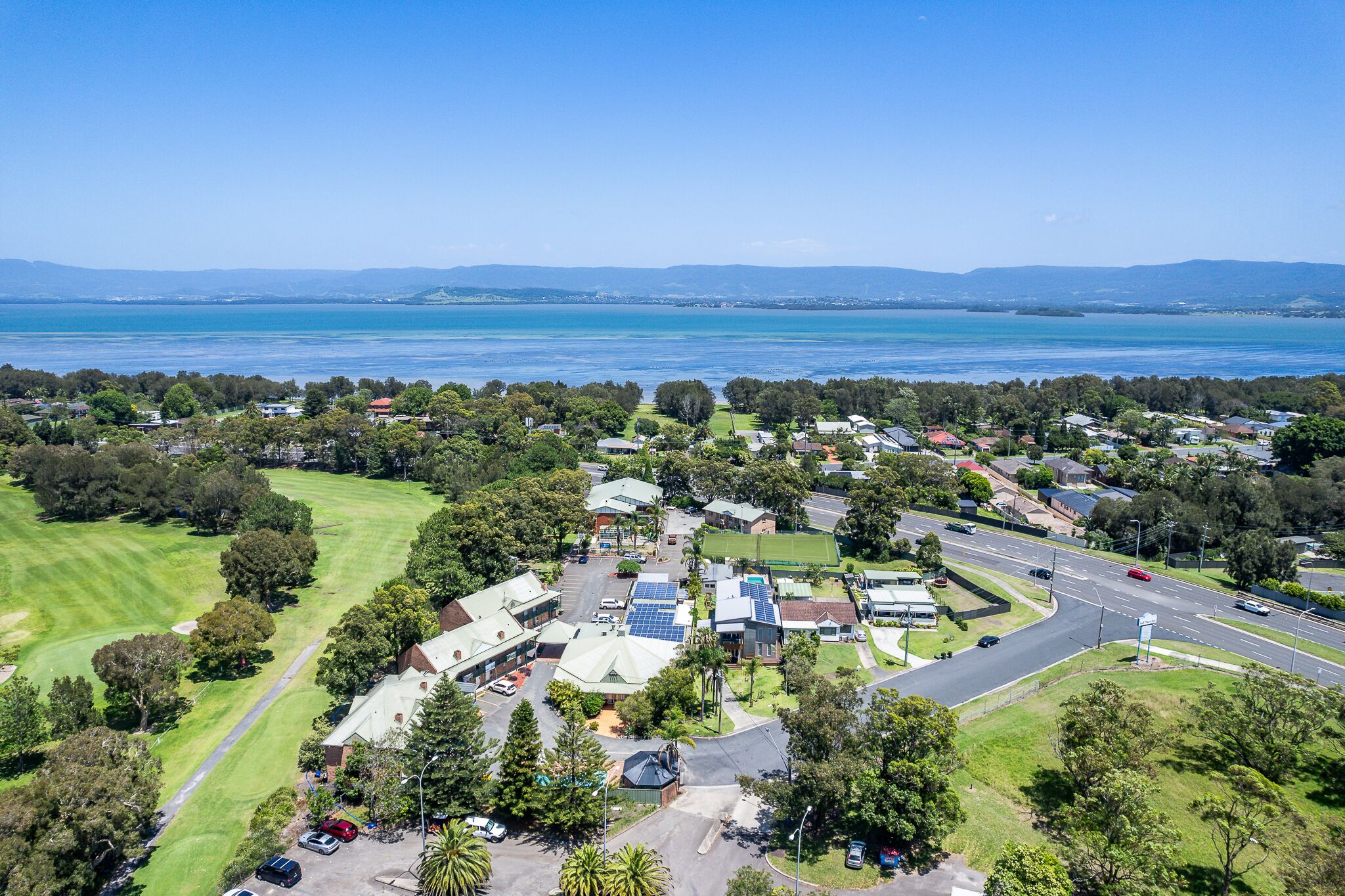 An aerial view of a residential area with houses, roads, and a large body of water in the background.