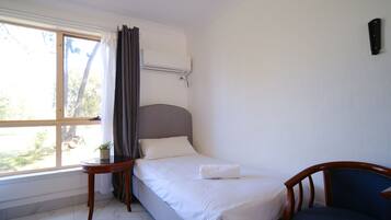 A hotel room with a bed, a chair, a small table with a plant, and a window with curtains.