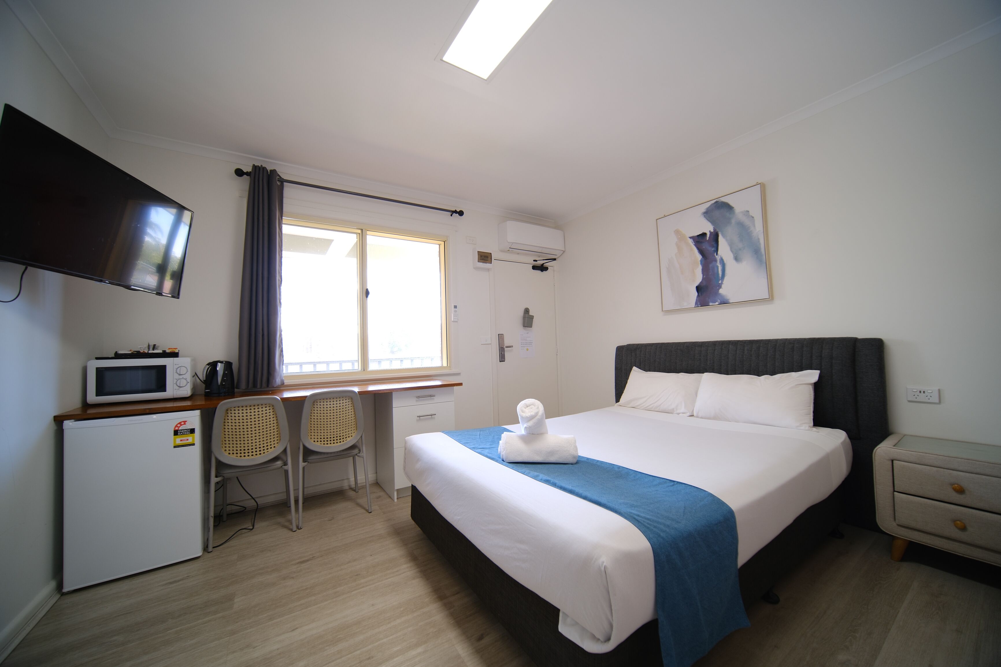 Una habitación de hotel con una cama, un escritorio con computadora, televisor y microondas.