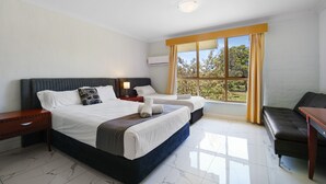 Habitación de hotel con una cama grande, dos mesitas de noche, un sofá y una ventana con cortinas.