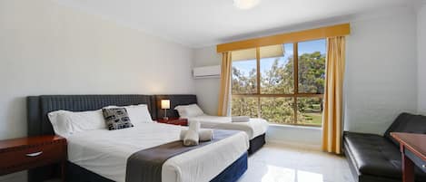 A hotel room with a large bed, two bedside tables, a sofa, and a window with curtains.