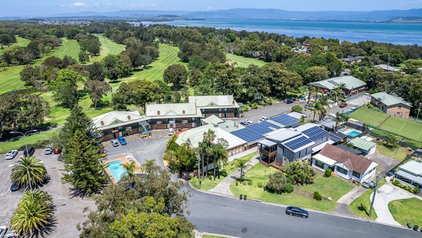 Vista aérea de una zona residencial con un edificio grande que cuenta con paneles solares, piscina y un césped bien cuidado.